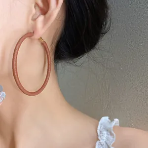 Close-up detail showing the texture of large brown leather-wrapped hoop earring on an ear