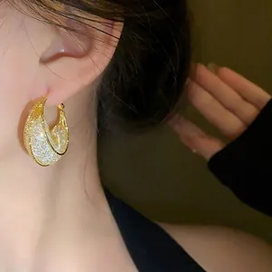 Elegant gold-tone mesh crescent hoop earrings shown being worn by a fashion model on ear.
