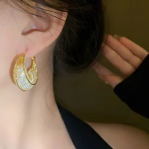 Detailed macro view of elegant golden mesh boat-shaped hoop earrings on a model ear