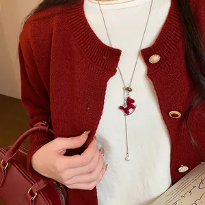 Nahaufnahme der roten beflockten Schaukelpferd-Halskette mit Perle auf rotem Pullover