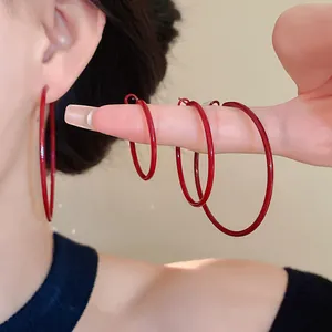 Close-up detail of deep red minimalist hoop earrings shown in three different sizes.