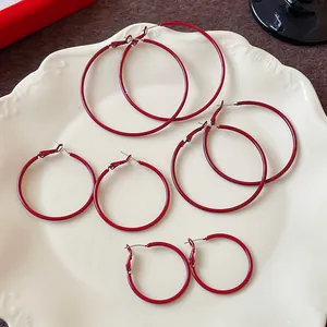 Set of four pairs of red minimalist hoop earrings in various sizes on a white plate.