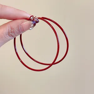 Close-up view of Ancora red oversized hoop earrings with silver needles shown by hand