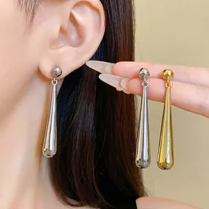Close-up of elegant gold and silver teardrop earrings on model's ear and hand.