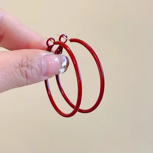 Close-up of large red Ancora hoop earrings with silver needles being held by hand