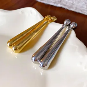 Detail shot of minimalist long water-drop earrings in gold and silver finishes.