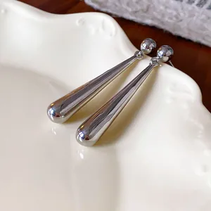 Close-up of minimalist silver metallic long water-drop dangle earrings on white plate