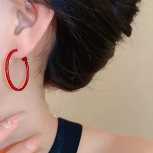 Close-up of stylish vibrant red hoop earrings worn by a model in a minimalist jewelry shot