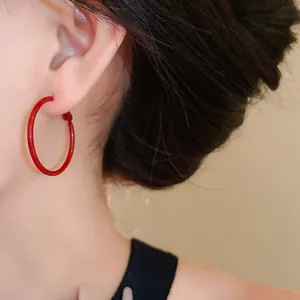 Detailed close-up of a vibrant red silver needle hoop earring worn on a model's ear