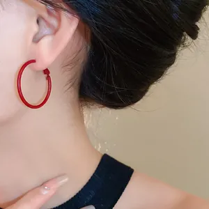 Close-up view of a minimalist large red hoop earring worn by a model from the side.