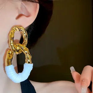 Primer plano de pendientes ovalados dorados con textura arrugada y detalles blancos