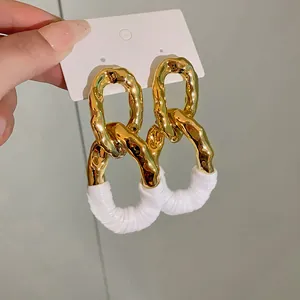 Primer plano de pendientes ovalados dorados con textura arrugada y detalle blanco