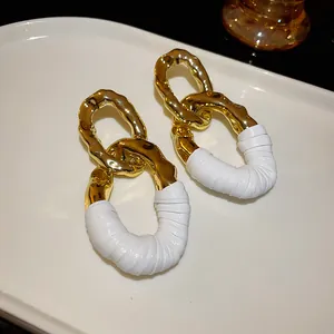 Primer plano de pendientes ovalados dorados con detalles de cuero blanco plisado