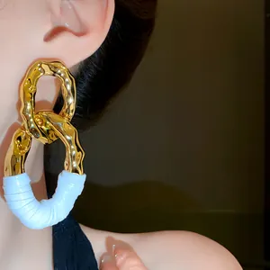 Primer plano de pendientes de eslabones ovales de metal dorado martillado y tela blanca