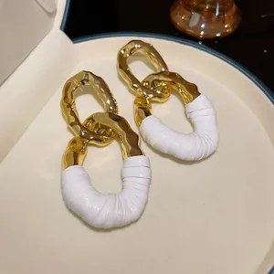 Primer plano de pendientes dorados con textura y un elegante diseño envuelto en cuero blanco.