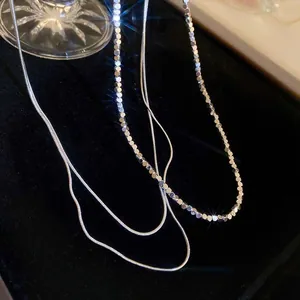 Close-up of shimmering silver geometric disk necklace and sleek snake chain on black velvet
