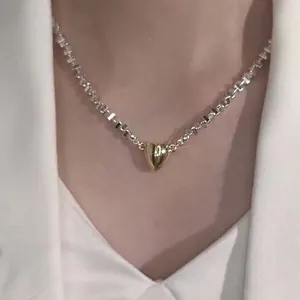 Close-up of a silver geometric link necklace featuring a gold heart-shaped pendant.