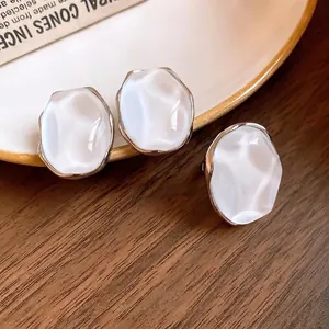 Minimalist pearlescent oval earrings with silver frames on a wooden background
