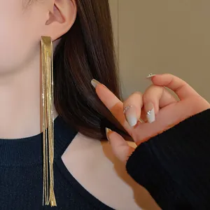 Detailed close-up of elegant long gold-plated tassel earrings worn on a model's ear.