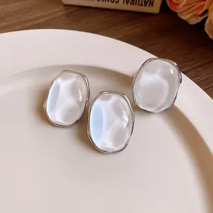 Macro view of pearlescent oval stud earrings with irregular silver metal edges on a plate