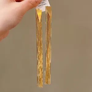 Close-up detail of elegant long gold-plated tassel earrings featuring modern triangular studs