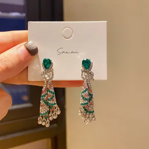 Close-up of ethnic style silver earrings with green teardrop stones and tassel detail.