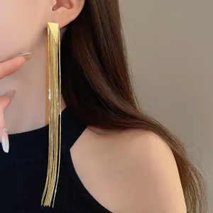 Close-up detail of long gold plated tassel earrings with triangle stud worn by model
