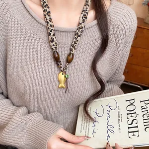 Dettaglio di collana in tessuto leopardato con ciondolo a forma di pesce dorato e perle