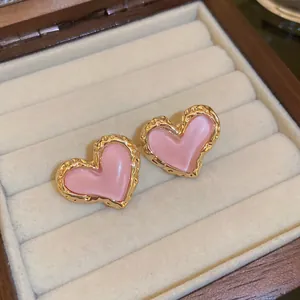 Elegantes pendientes de corazón rosa con borde dorado texturizado en un joyero de terciopelo
