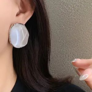 Macro view of pearlescent oval stud earring with a glossy silver border shown on ear