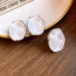 Detail view of pearlescent oval stud earrings with an organic ripple texture and silver rim