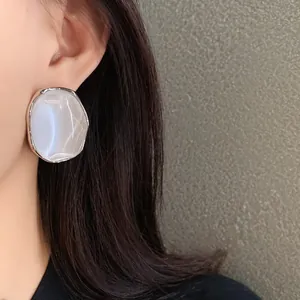 Detailed close-up view of a pearlescent oval earring with silver edge worn on ear