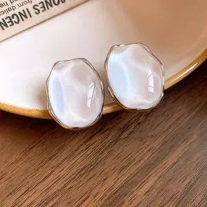 Macro detail of minimalist pearlescent white oval stud earrings with silver-toned metal borders