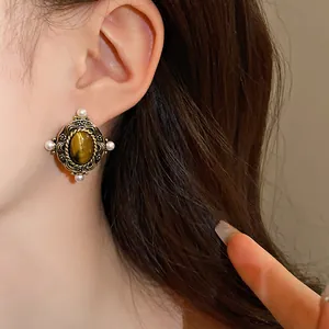 Detail of vintage court style earrings with tiger's eye stone and pearls on model's ear.