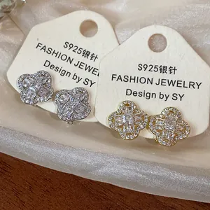 Detail of clover-shaped zircon ear clips in silver and gold finishes on display cards.