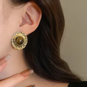 Close-up detail of a vintage gold-tone tiger eye stud earring worn on a model's ear