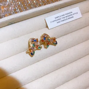 Vista macro di orecchini a perno a farfalla con zirconi colorati su velluto beige