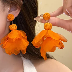 Primo piano di orecchini pendenti a fiore in rafia e chiffon arancione per stile vacanza.