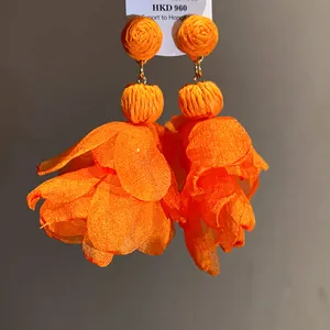 Primo piano di orecchini a fiore in chiffon arancione con dettagli in rafia per vacanze.