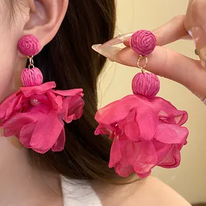 Dettaglio di orecchini a fiore in chiffon fucsia con perni in rafia intrecciata