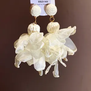 Primo piano di orecchini a fiore in chiffon color crema con dettagli in rafia intrecciata.