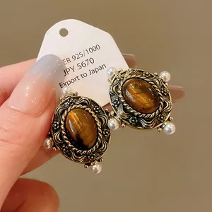 Detailed macro view of vintage court style tiger eye earrings with pearls and ornate gold frame.