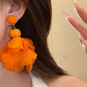 Dettaglio di orecchini pendenti a fiore in rafia e chiffon arancione per stile vacanza
