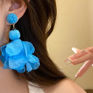 Primo piano di un orecchino pendente con fiore in chiffon e rafia blu indossato da una modella