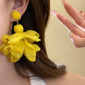 Dettaglio di orecchini pendenti in rafia gialla e fiori di chiffon sull'orecchio