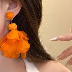 Primo piano di grandi orecchini a fiore in chiffon arancione indossati da una modella