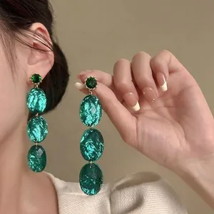 Emerald green oval dangle earrings with shimmering zircon studs shown on a model's ear