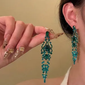 Detailed view of elegant long dangling emerald green crystal earrings with gold finish.