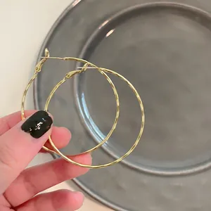 Detailed macro view of large textured gold hoop earrings held by a hand for scale and style