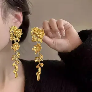 Detailed macro view of elegant matte gold long dangle earrings featuring floral and leaf motifs
